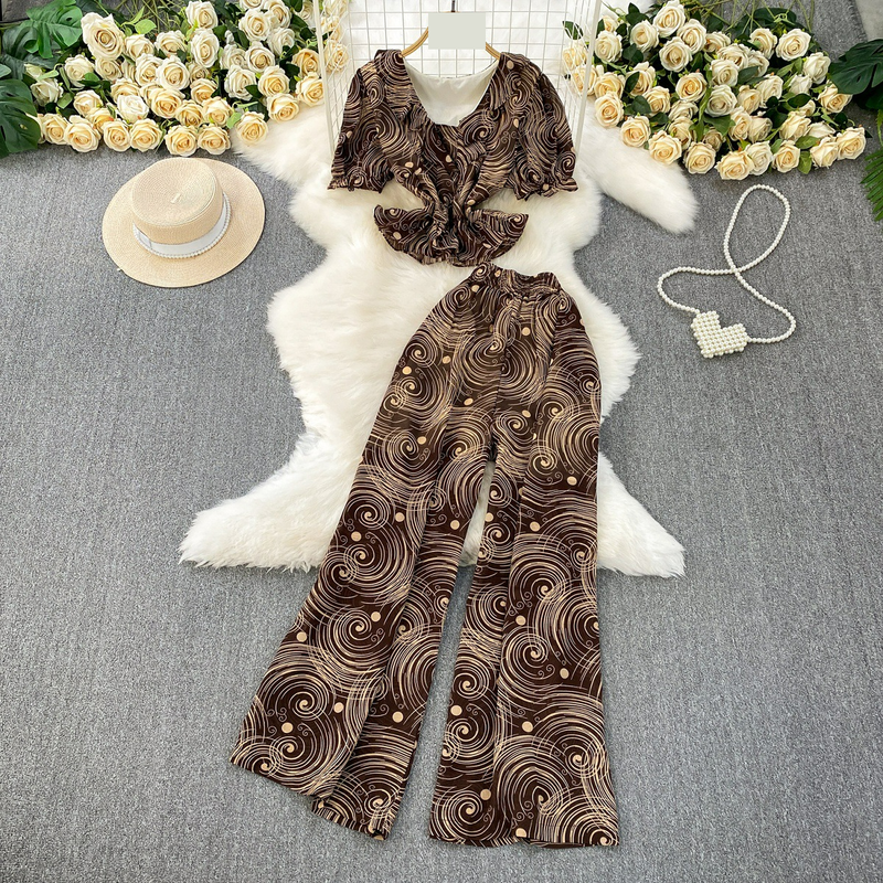 Completo leggero e maturo, snellente, composto da una maglietta a maniche corte con scollo a V e volant e pantaloni larghi e dritti in chiffon stampato a vita alta. Completo due pezzi._voghion.com